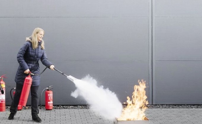 A woman in a blue coat using a CO2 fire extinguisher on a controlled fire during a training session.